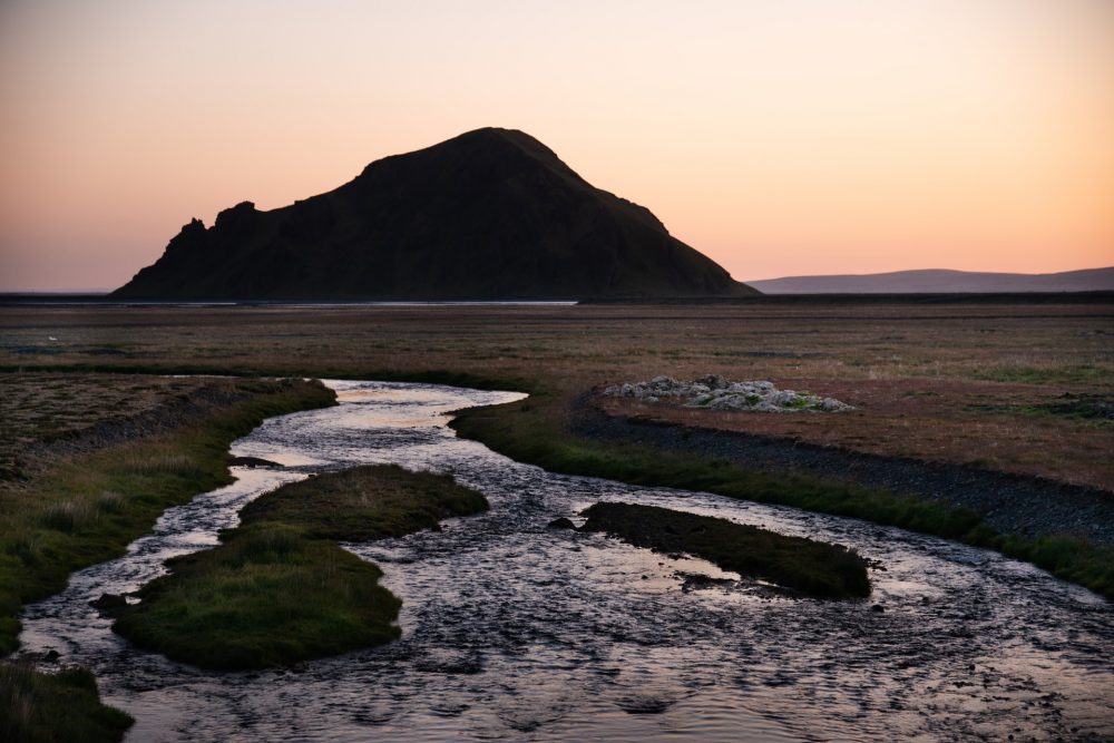 The melt water from the glaciers of Iceland passes over a low grassy pain under the midnight sun of the far north.